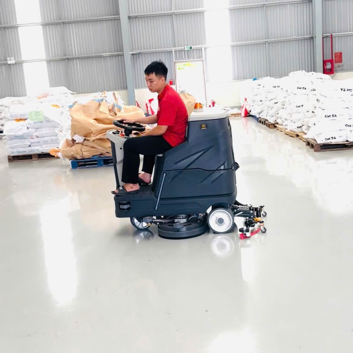 Máy chà sàn ngồi lái Krapo M2913 Krapo M2913 đang di chuyển trên sàn bê tông sáng bóng, một công nhân ở hậu cảnh.
